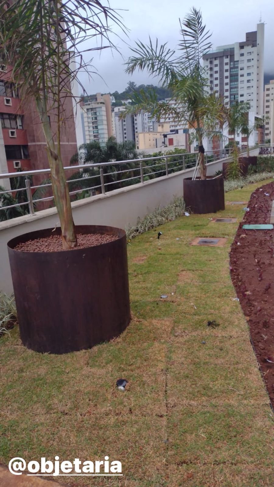 Vaso de Aço Corten 3 Vaso de aço corten sob medida em formato cilíndrico grande instalado em jardim corporativo.