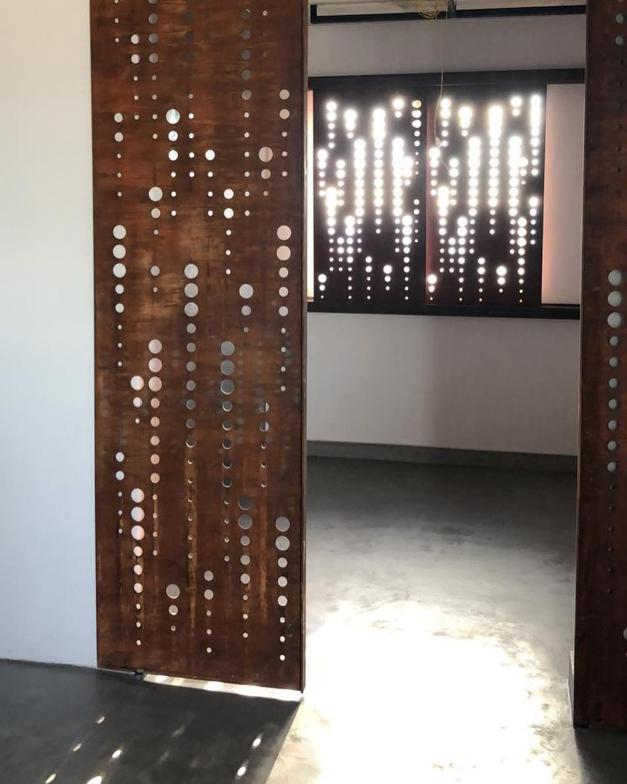 Divisória vazada deslizante em aço corten com padrão de pontos luminosos