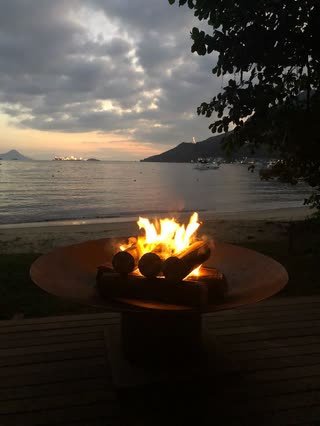 Lareira externa de chão em aço corten acesa ao anoitecer em deck à beira-mar