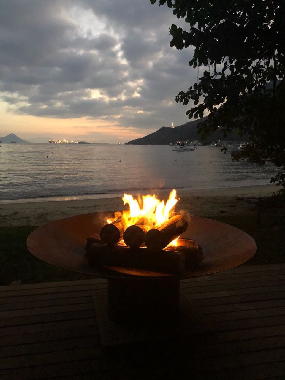 Lareira externa de chão em aço corten acesa ao anoitecer em deck à beira-mar