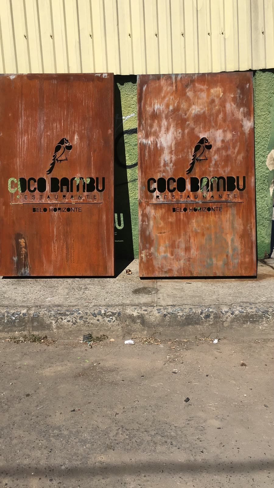 Duas placas em aço corten com a mesma logomarca vazada, apoiadas em um muro antes da instalação